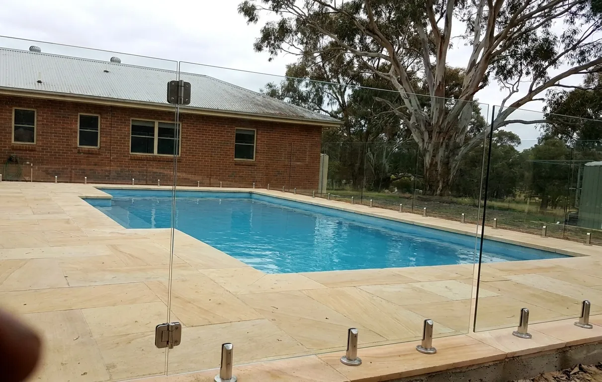 Frameless glass pool fence on spigots around a backyard swimming pool